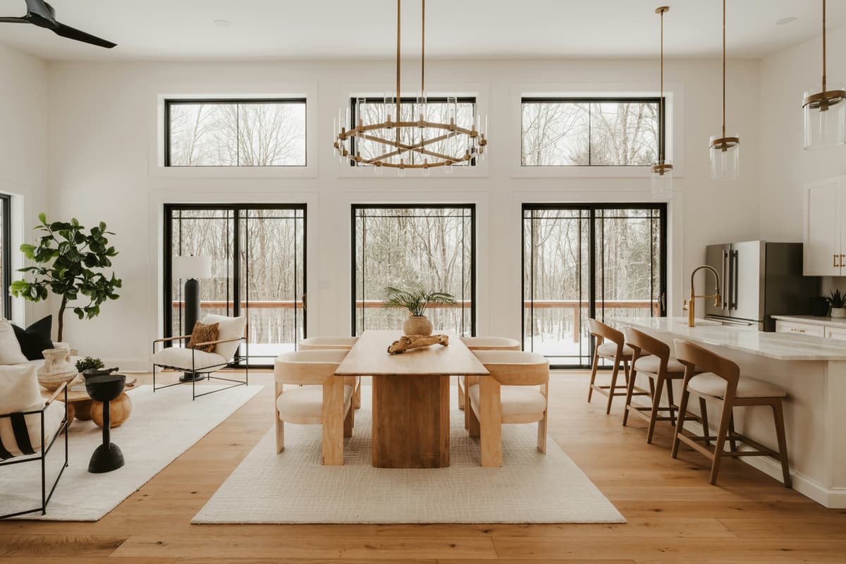 A bright open living and dining room with large windows, a wood dining table and a kitchen island