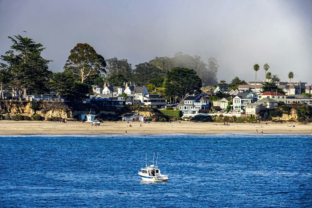 Homes on the bluffs above a beach on the Monterey Bay coast, with a boat on the water